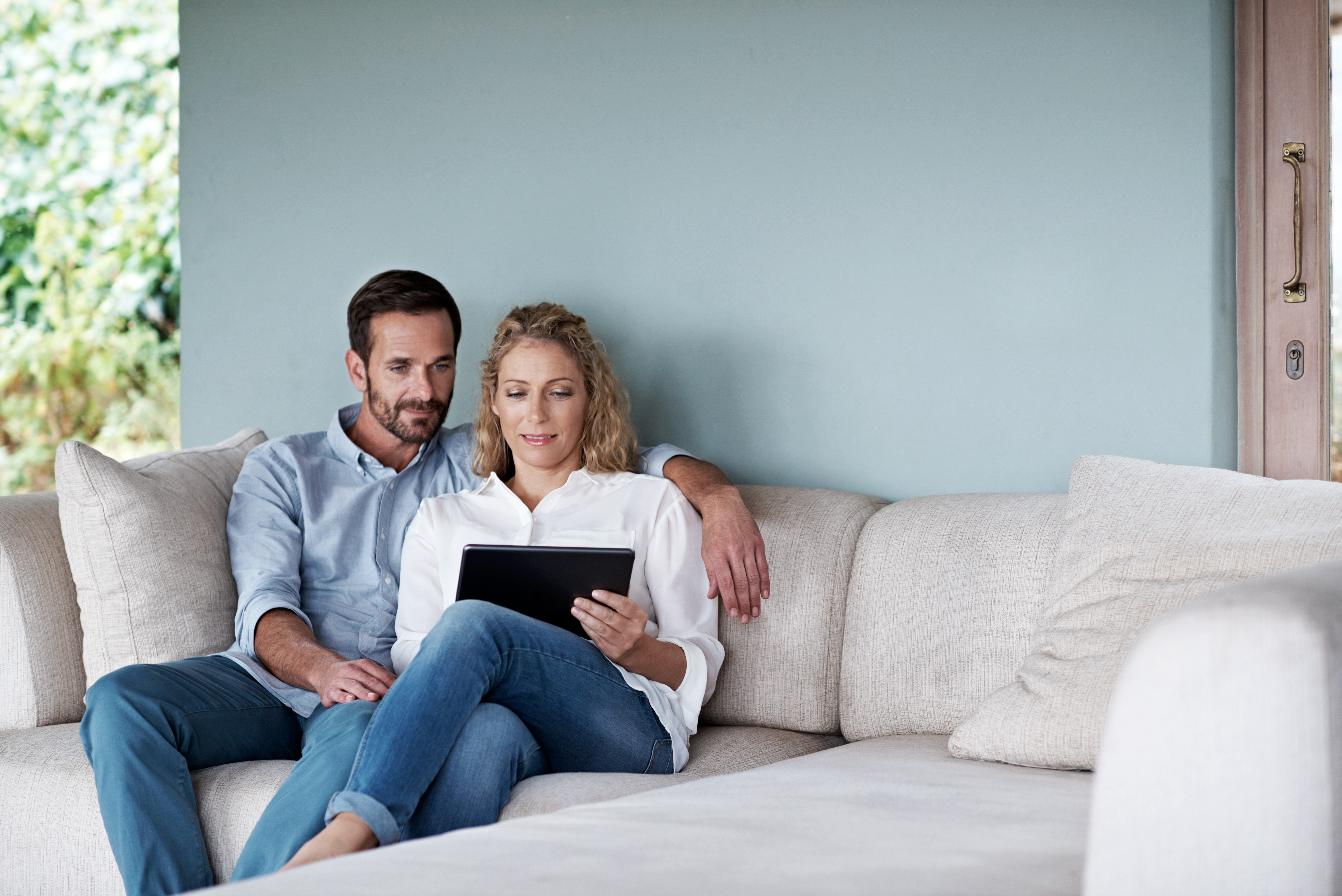 Couple sitting on couch browsing on their tablet